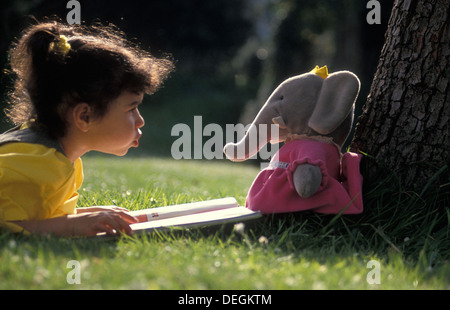 kleine Mädchen-Lesebuch, Spielzeug-Elefanten im freien Stockfoto
