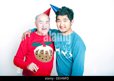 Porträt eines älteren Erwachsenen Mann ein jungen asiatischen Mann tragen Weihnachten Jumper Partyhüte Stockfoto