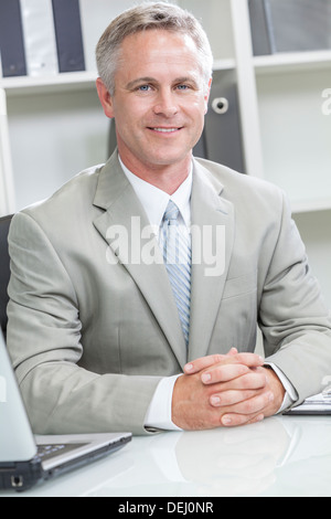 Glücklich lächelnden Mann oder Geschäftsmann sitzt am Schreibtisch im modernen Büro Stockfoto