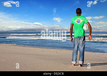 Hintere Ansicht Mann stehend tragen brasilianischen t-Shirt mit Fußball am Strand Stockfoto