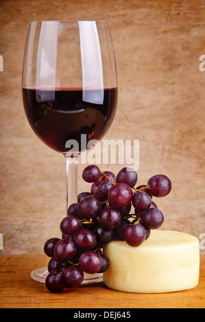 Stillleben mit Glas Rotwein, Trauben und Käse auf einem hölzernen Vintage-Hintergrund Stockfoto