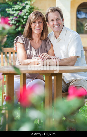 Attraktive, romantische & glücklich mittleren gealterten Mann und Frau Paar in den Vierzigern, draußen zu sitzen zusammen im Garten mit Blumen Stockfoto