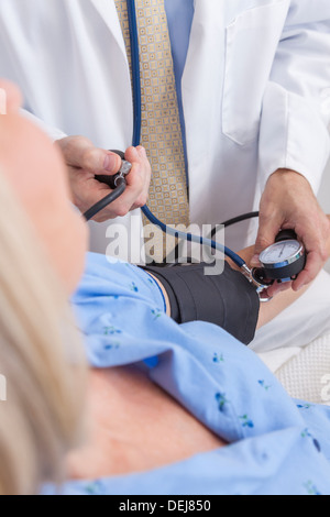 Ältere Frau Patienten im Krankenhausbett mit Blutdruck von männlichen Arzt getroffen Stockfoto