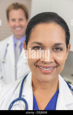 Eine Latina hispanische Ärztin im weißen Kittel mit Stethoskop & männlicher Kollege hinter ihr Stockfoto
