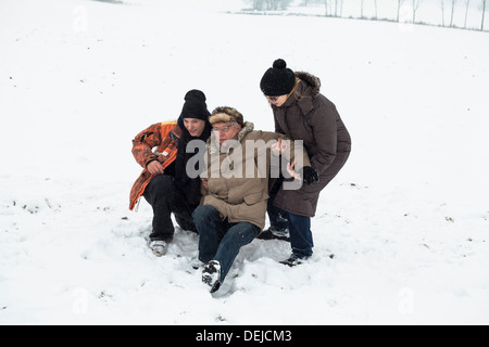 Paar der jungen Menschen hilft, senior Mann aufstehen nach Unfall auf Schnee. Stockfoto