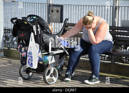 Frau sitzt satt, mit Baby im Kinderwagen, Paignton, Devon, England, UK Stockfoto