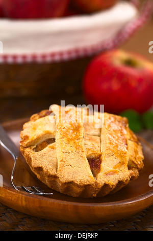 Kleine Runde Apfelkuchen mit Gitter Kruste auf Holzplatte mit Kuchengabel, in den Rücken, einen Apfel und ein Korb mit Äpfeln Stockfoto