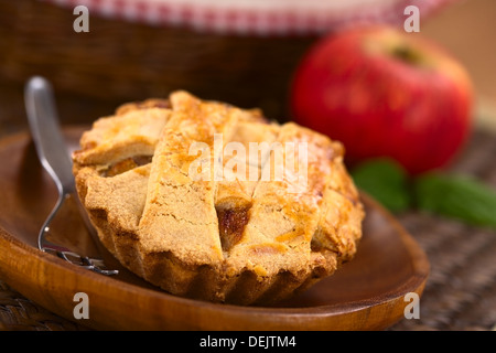 Kleine Runde Apfelkuchen mit Gitter Kruste auf Holzplatte mit Kuchengabel, in den Rücken, einen Apfel und einen Korb Stockfoto