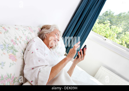 Glücklich senior Frau mit Handy-Bett zu Hause Stockfoto