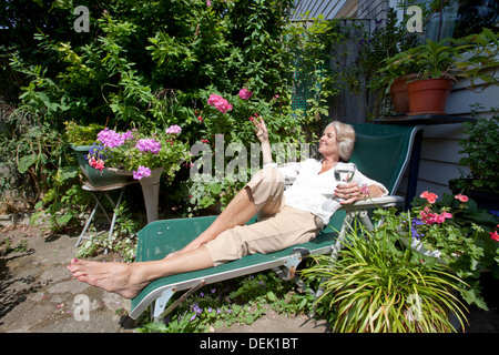 Ältere Frau mit Weinglas entspannende Lounge Sessel Garten Stockfoto