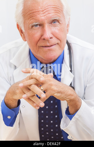 Ein senior woman männlichen medizinischen Klinik Arzt sitzen an einem Schreibtisch in einem Hemd, Krawatte und Stethoskop Stockfoto