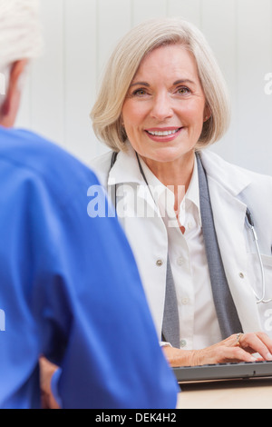 Eine ältere weibliche Ärztin sitzen an einem Schreibtisch trägt einen Anzug und Stethoskop im Gespräch mit einem älteren männlichen Patienten Stockfoto