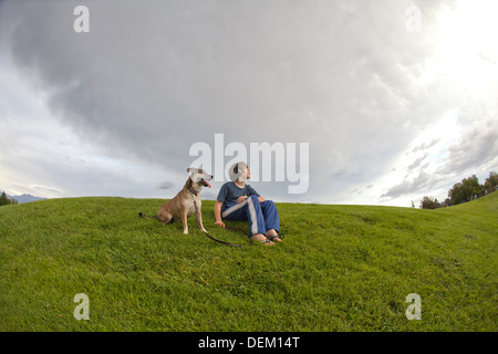 Zehn Jahre alter Junge sitzt auf einem Hügel mit seinem Hund Sturm Wolken. Stockfoto