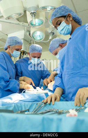 Interracial Team Ärzte männlichen weiblichen Chirurgen in der Chirurgie auf Patienten mit im Theater tragen scheuert & Masken Stockfoto