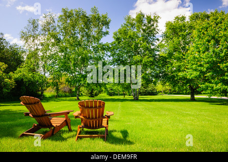 Zwei hölzerne Adirondack Stühle auf üppig grüne Wiese mit Bäumen Stockfoto