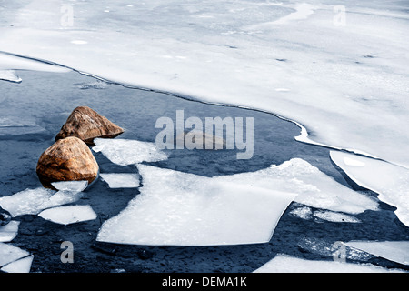 Gebrochenes Eis schwimmt auf Wasser im kalten Seeufer mit Felsen im winter Stockfoto