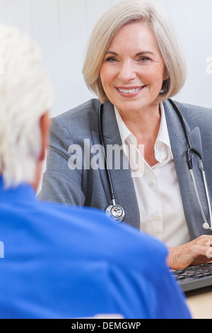 Eine ältere weibliche Ärztin sitzen an einem Schreibtisch trägt einen Anzug und Stethoskop im Gespräch mit einem älteren männlichen Patienten Stockfoto