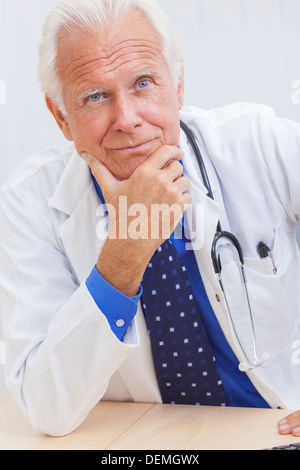 Ein senior männlichen Arzt sitzen an einem Schreibtisch in einem Büro mit Computer und trug ein Hemd, Krawatte und Stethoskop Stockfoto