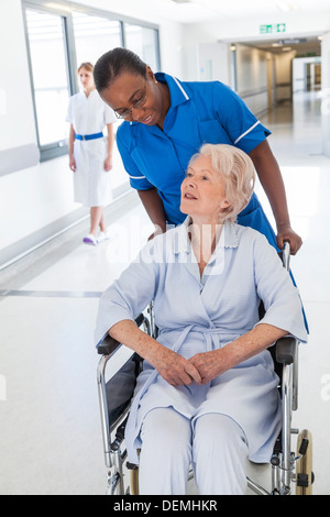 Ältere weibliche Frau Patienten im Rollstuhl sitzend im Krankenhausflur mit afroamerikanischen Krankenschwester Stockfoto