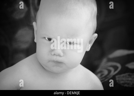 Lustige böse Baby Mädchen Nahaufnahme monochrome Portrait auf dunklen Hintergrund jedoch unscharf Stockfoto