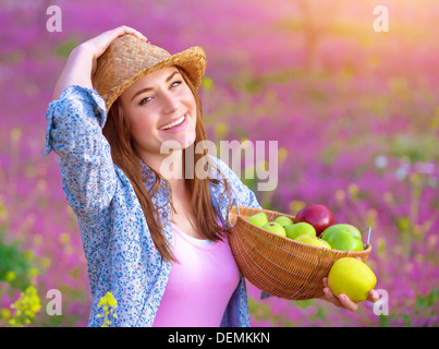 Closeup Portrait der hübsche Frau mit Korb Äpfel, Picknick auf rosa Blumen Wiese, Erntezeit, Gartenarbeit Konzept Stockfoto