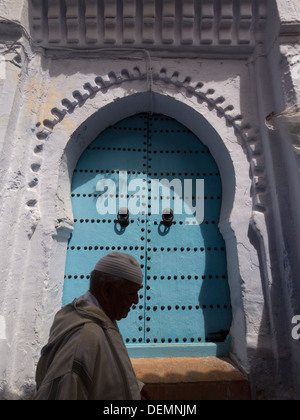 Alter Mann vor einem geschlossenen blauen Holztür in Chefchaouen, Marokko Stockfoto