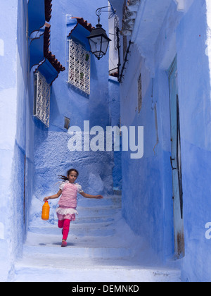 Junge Mädchen laufen auf einer Straße mit blau gestrichenen Häuser in Chefchaouen, Marokko Stockfoto