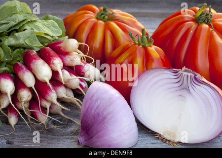 Coeur de Boeuf Tomaten, große rote Zwiebeln und Radieschen frisch vom Wochenmarkt auf einem alten Holztisch Stockfoto