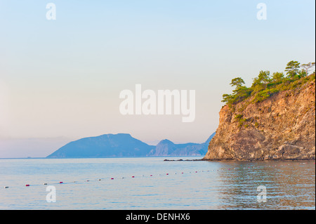 wachsende Bäume an einem steilen felsigen Küstenstreifen bei ruhiger See Stockfoto