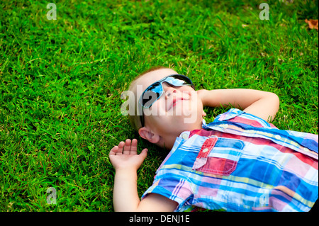 glückliche kleine Junge liegend ruhen auf dem grünen Rasen in Sonnenbrillen Stockfoto