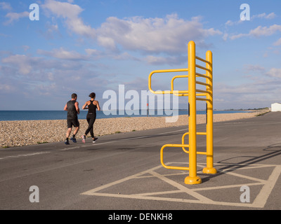 Zwei Leute Joggen entlang der Strandpromenade mit Verkleidung trail Apparate im Aldwick Bognor Regis West Sussex England Großbritannien Großbritannien Stockfoto