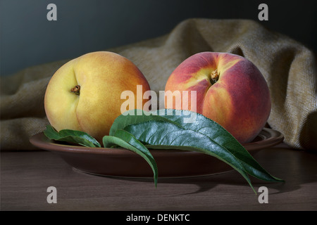 Zwei Reife Pfirsich mit Blättern auf einer Keramikplatte Stockfoto