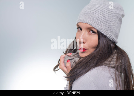 Hübsche junge Frau im Winter kuscheln sich in ihre wolligen grau Mode Strick Jersey, Schal und Mütze an einem kalten Tag Stockfoto