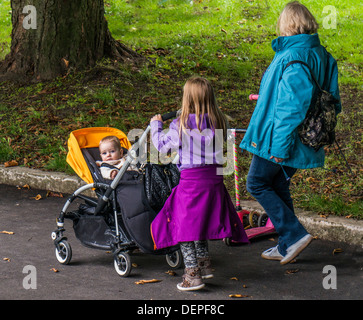 Eine Familie, die zu Fuß in den Park mit einem kleinen Kind im Buggy starrte in die Kamera, Crystal Palace Park, London England. Stockfoto