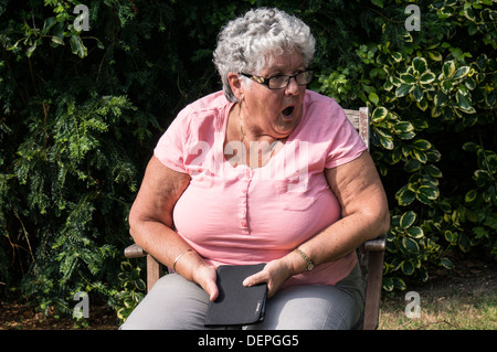 Ein geschockt Alt/Senioren/ältere Dame (Alter 76) sitzen in einem Stuhl in Ihrem Garten. Stockfoto