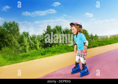 Cute glücklich lachen dich wenig Jahre junge Inline-Skating Skaten bergab im Park an sonnigen Sommertag Stockfoto