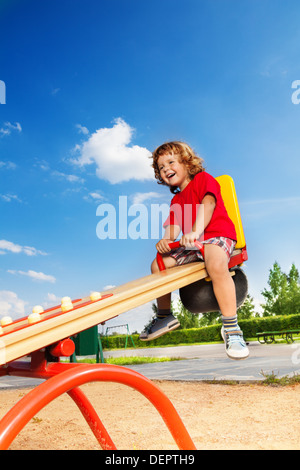 Glücklich Lauging kleine dreijährige Kind sitzt auf der Wippe Stockfoto