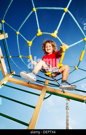 Glückliche kleine drei Jahre alte Kind Junge kletterte auf Seil Web auf Spielplatz blickte und lachen Stockfoto