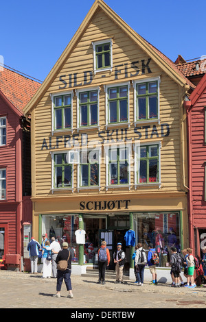 Touristen, die durch ein Geschäft mit norwegischen Geschenke in alten traditionellen hölzernen Gebäude in Bryggen, Bergen, Hordaland, Norwegen, Skandinavien Stockfoto