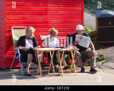 Ein Mann und zwei Frauen lesen Sie ihre Zeitung in angenehmen Spätsommer-Sonne durch eine rote Strandhütte in Whitby Stockfoto