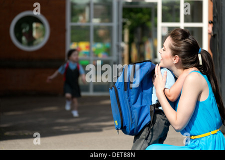 Eine attraktive junge Mutter beruhigend auf glücklich & Abholung oder Abwurf ihres Sohnes vor den Toren der Vorschule Stockfoto