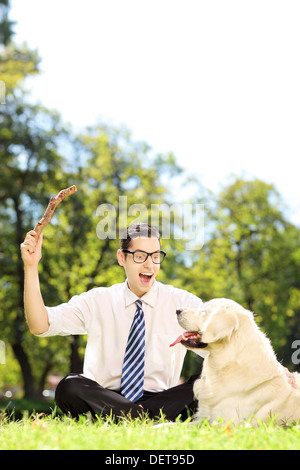 Mann mit Krawatte und Brille sitzt auf einem grünen Rasen spielen mit Hund in einem park Stockfoto