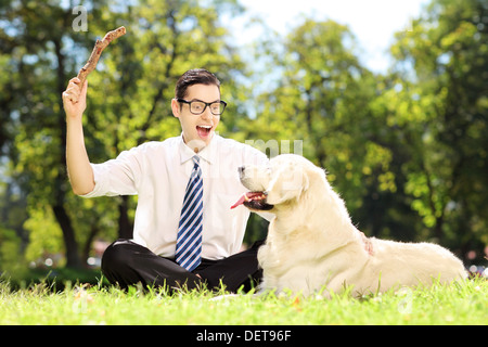 Mann mit Krawatte und Gläser auf einer grünen Wiese sitzen und spielen mit Hund in einem park Stockfoto