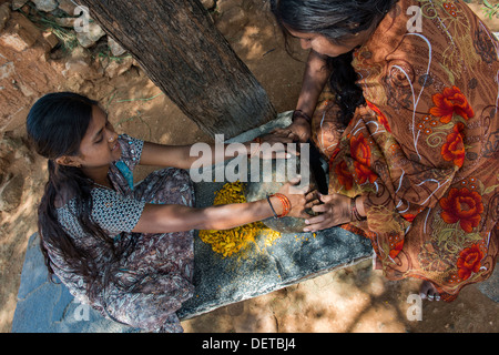 Zwei indische Frauen zerkleinern Kurkuma Wurzeln zu Pulver mit einem runden Stein in einem indischen Dorf. Andhra Pradesh, Indien Stockfoto