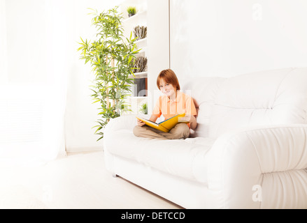 Smart lächelnd kaukasischen junge Porträt im Innenraum auf dem Sofa zu Hause sitzen und lesen Stockfoto