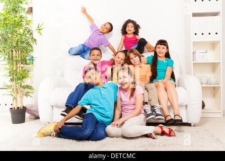 Große Gruppe von acht Kinder, Jungen und Mädchen, Freunde, Schule Alter, mit schwarzer und weißer Hautfarbe, umarmen, Lächeln und Lachen das Sitzen auf dem Boden und an den Trainer im Wohnzimmer zu Hause Stockfoto