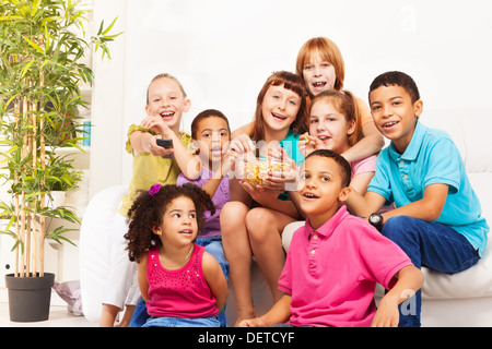 Gruppe der Vielfalt suchen Kinder, Jungen und Mädchen sitzen auf der Coach, Lachen, wechseln Sie die Kanäle auf dem Fernseher und Popcorn essen und dabei auf Film Stockfoto