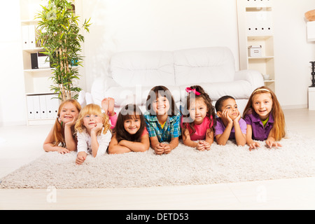 Gruppe der Acht kleinen Kindern, Jungen und Mädchen, Asiatische und Kaukasischen am Boden zu Hause im Wohnzimmer an Kamera suchen mit Sofa auf Hintergrund Stockfoto