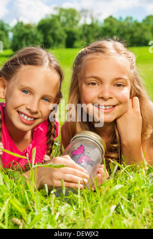 Close-up Portrait glücklichen kleinen neun Jahre alten Mädchen Freunde jar halten mit Schmetterling mit in das Gras und zeigt großen Lächeln auf glückliche Gesichter Stockfoto