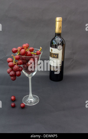 Flasche Rotwein und einem Glas roten Trauben auf schwarzem Hintergrund Stockfoto